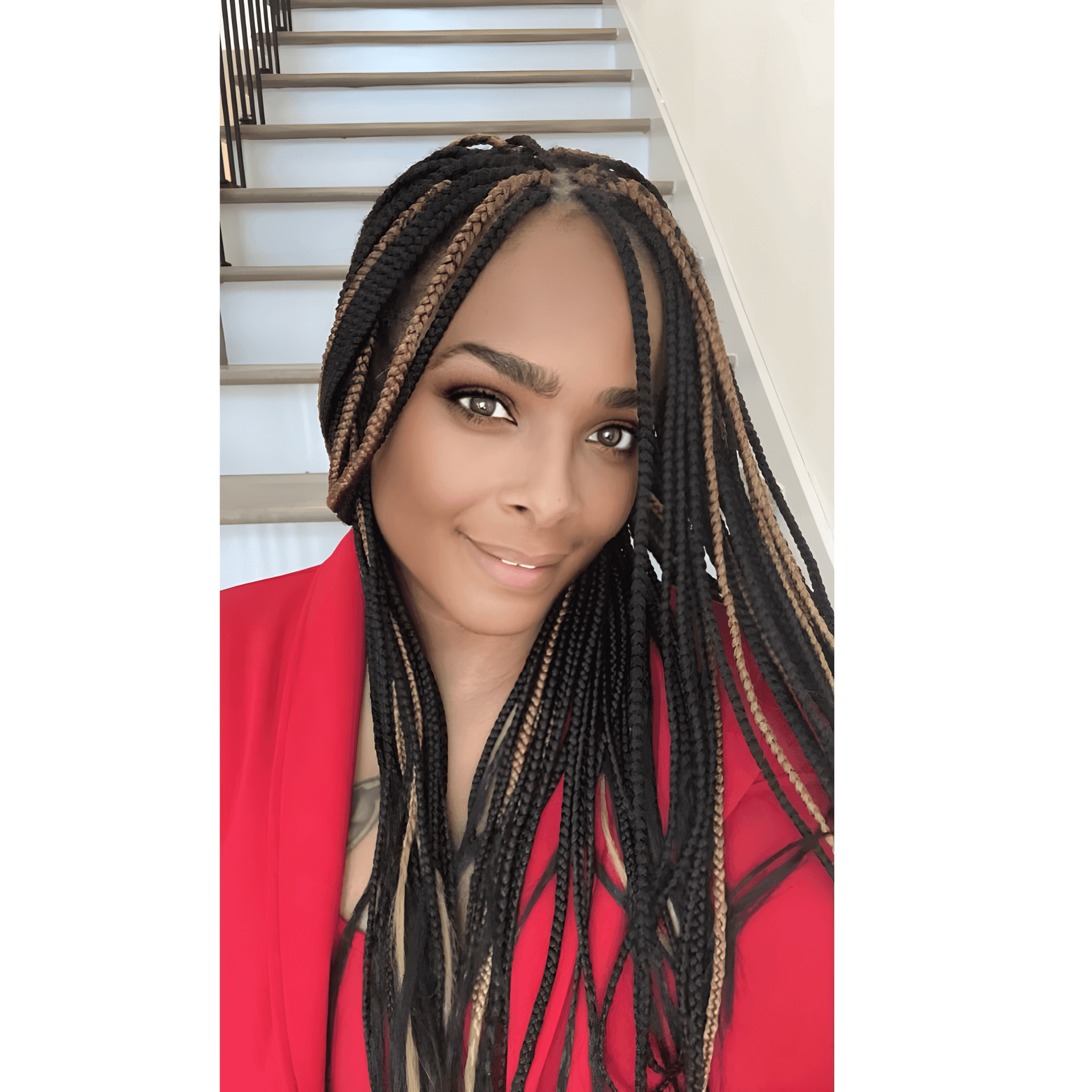 Person with long braids wearing a red jacket, smiling in front of a staircase.