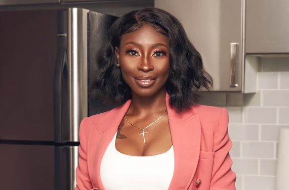 Woman with shoulder-length hair wearing a coral blazer and white top, standing in a modern kitchen.