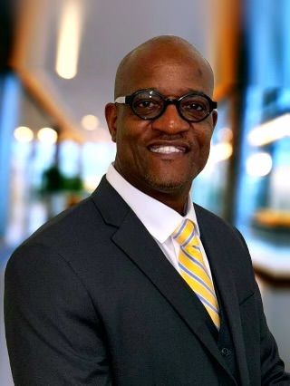 Person in a business suit with a yellow striped tie standing in a modern, brightly lit hallway.